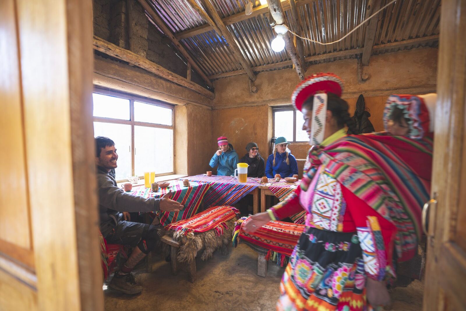Una mujer quechua con ropa tradicional recibe a los invitados en una casa de adobe