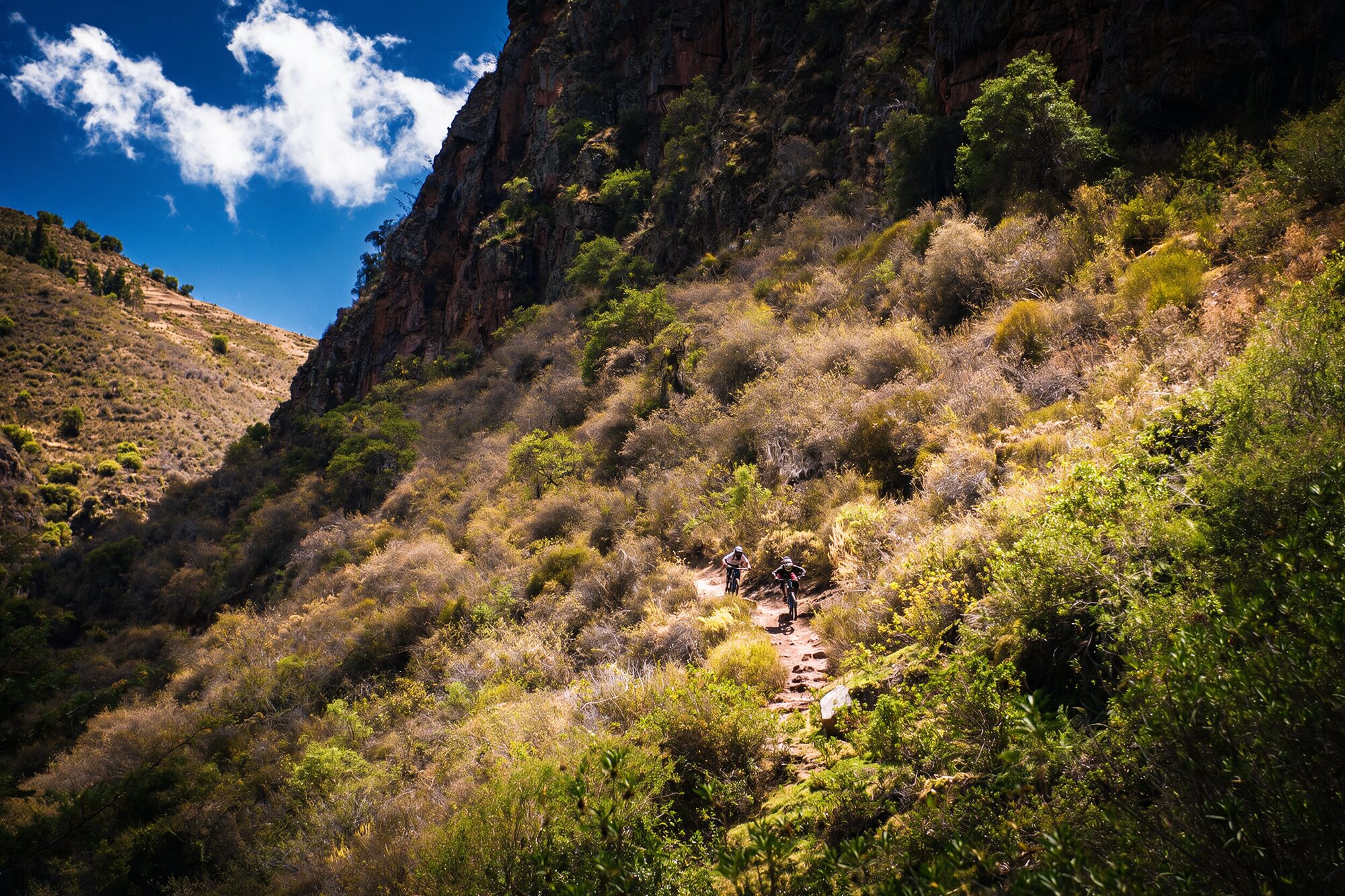 Singletrack cut into the canyon wall, the Sacred Valley sky above